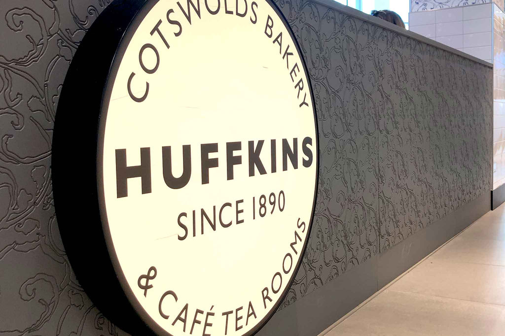 Huffkins Cotswolds Bakery & Cafe Tea Rooms backlit logo on grey wall
