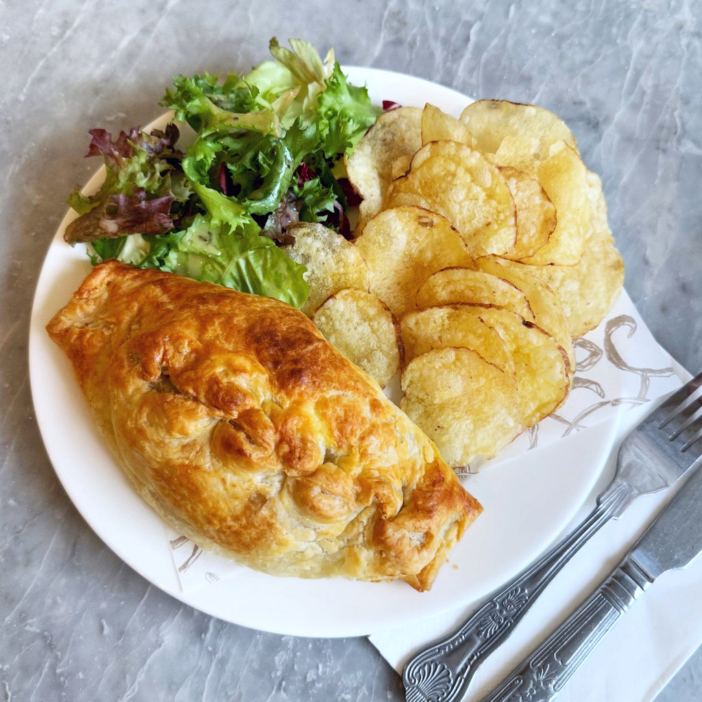 Freshly baked pasty with side salad and crisps on a plate with cutlery